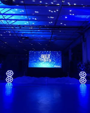 Scenografia natalizia in blu con un grande schermo LED che annuncia il “Xmas Family Day”, giochi di luce sul soffitto e decorazioni geometriche illuminate ai lati del palco.